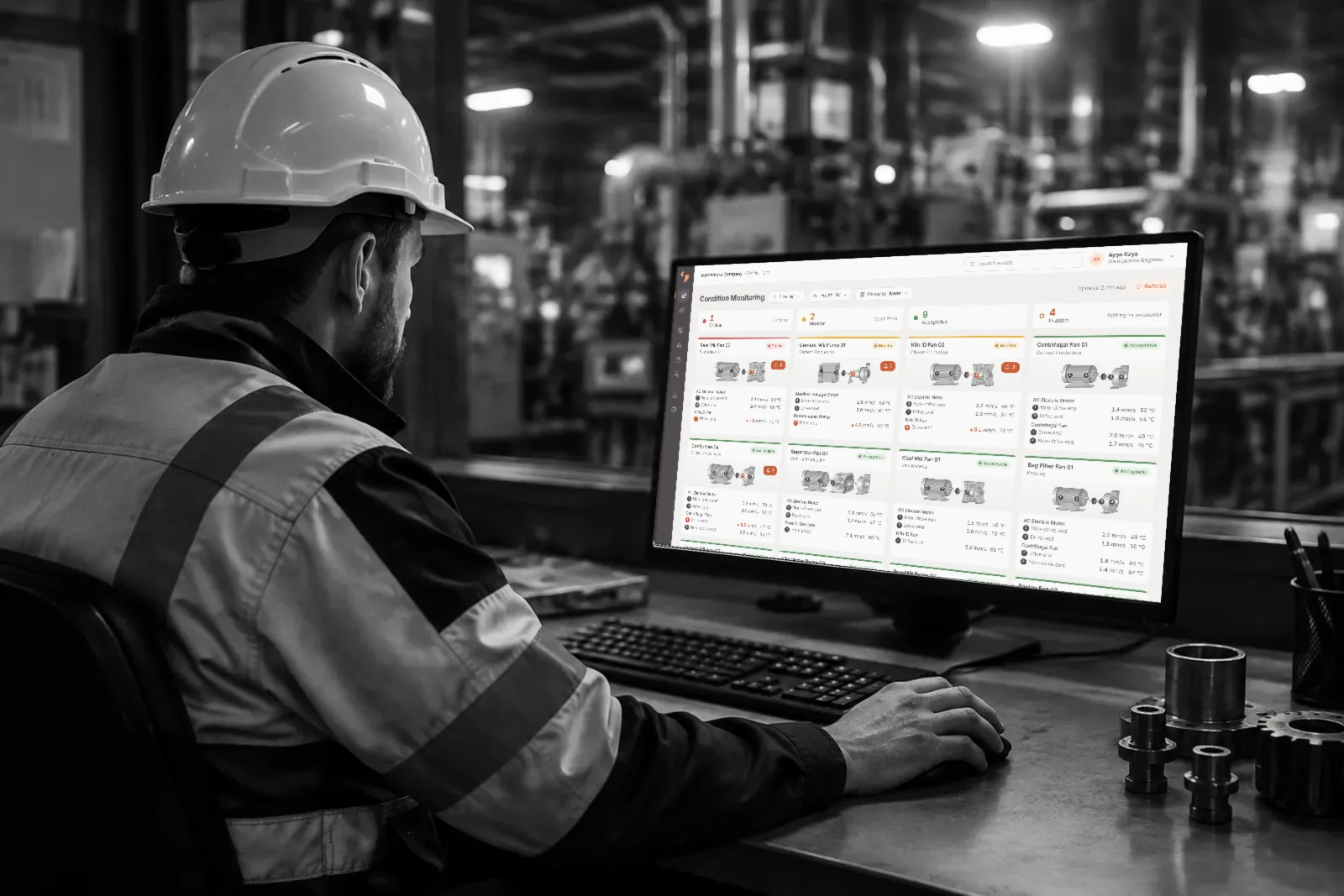 A maintenance engineer in a hard hat at a factory control desk, looking at LAKE's new Condition Monitoring screen on a large monitor
